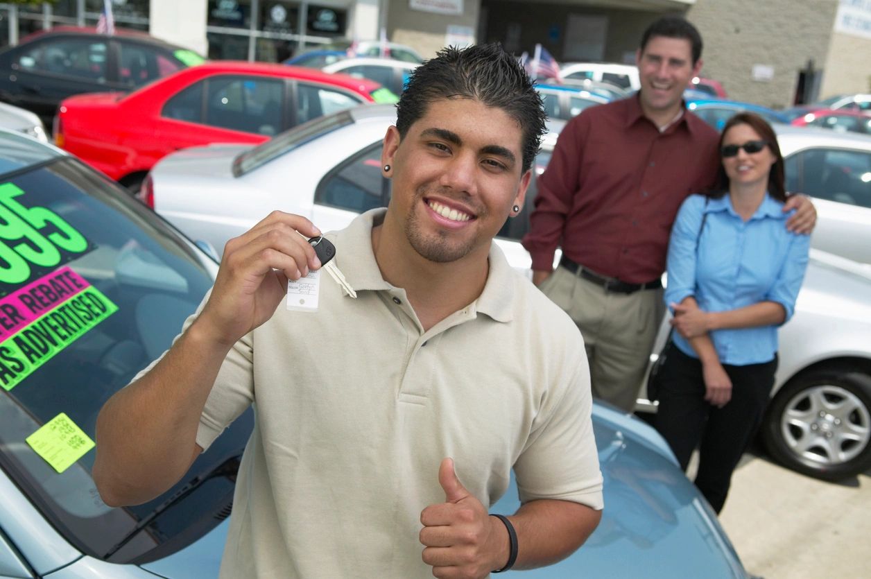 A man holding up his new car keys in front of some people.