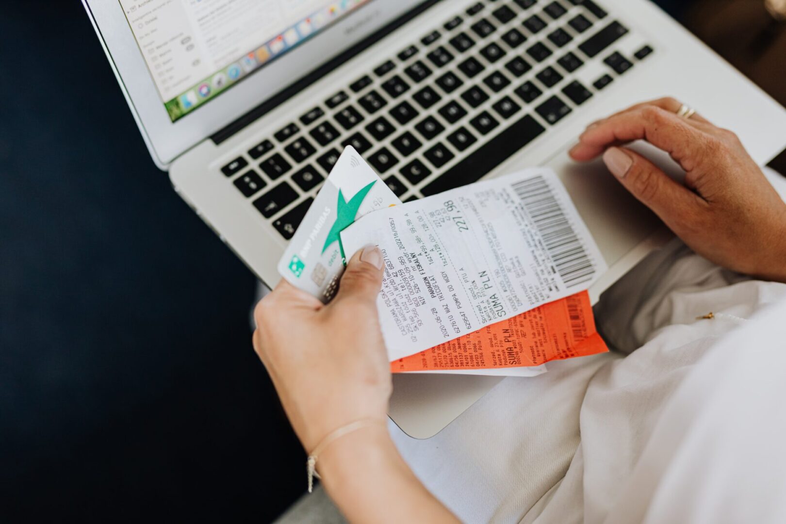 A person holding an airplane ticket and using a laptop.